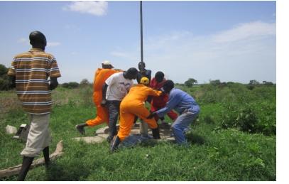 A community team works on a borehole in green fields